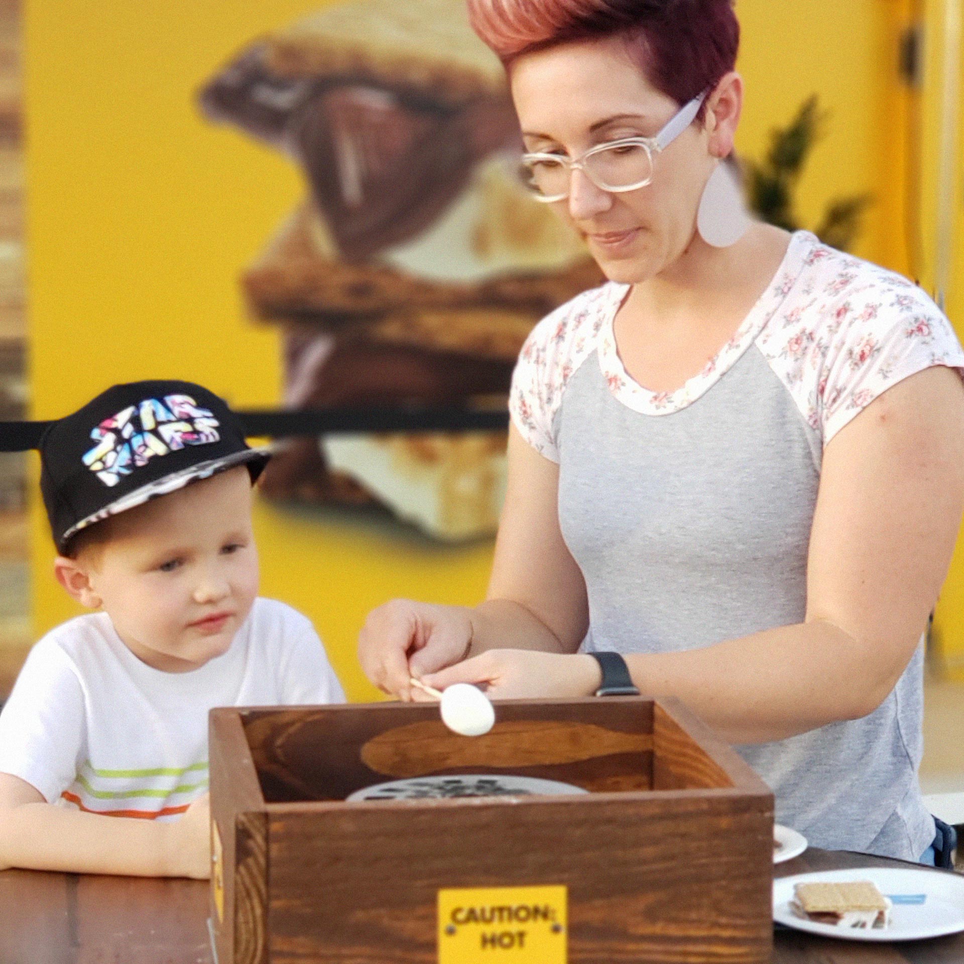 A mom and her son hold a marshmallow over a heat plate using a skewer 